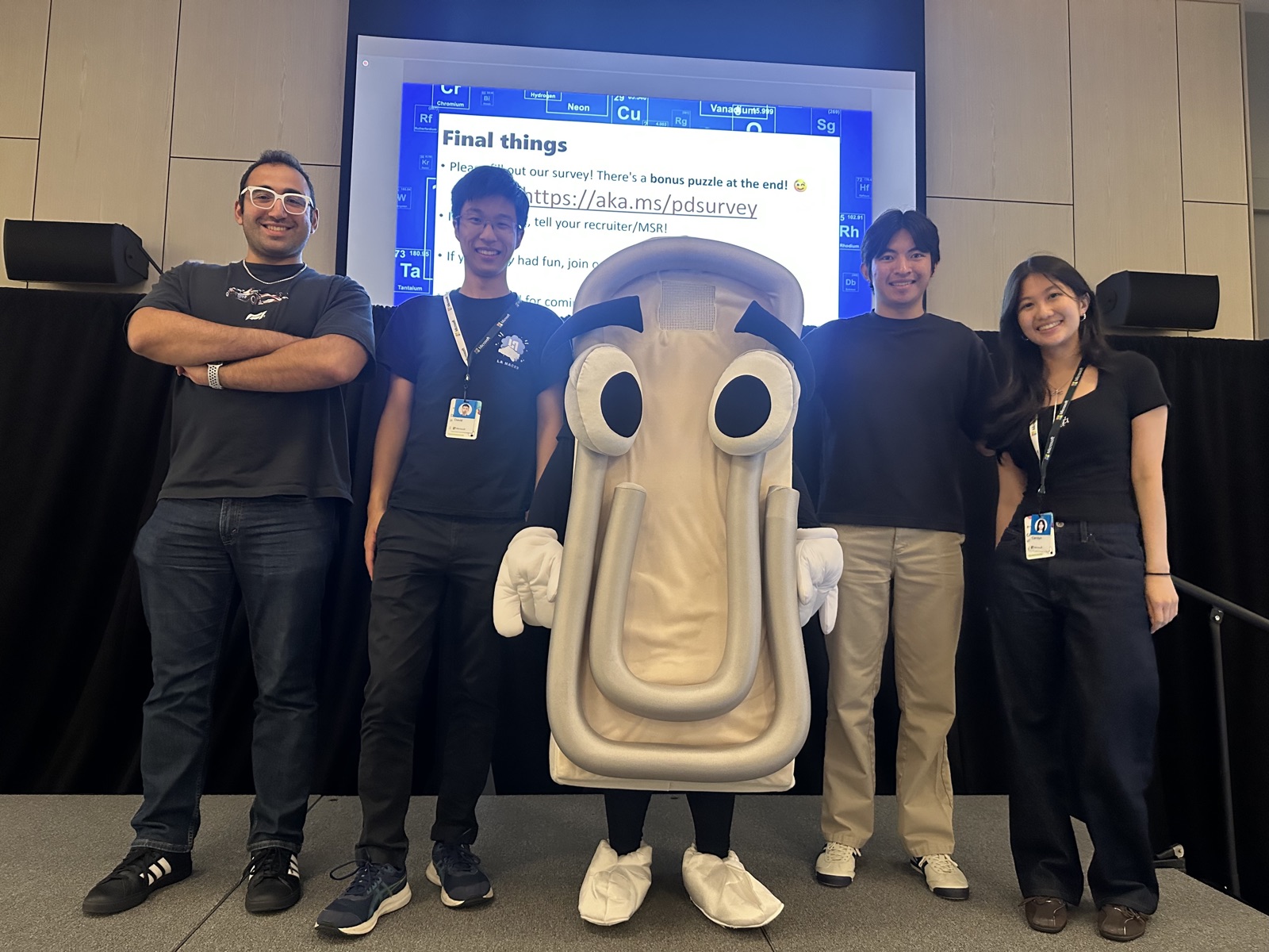 Interns on stage with the Clippy mascot at the end of intern puzzle day